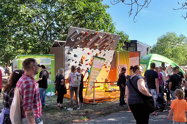 Foto mit Menschen und FROHE ZUKUNFT-Stand mit Kletterwand beim Pestalozzi Parkfest in Halle (Saale)