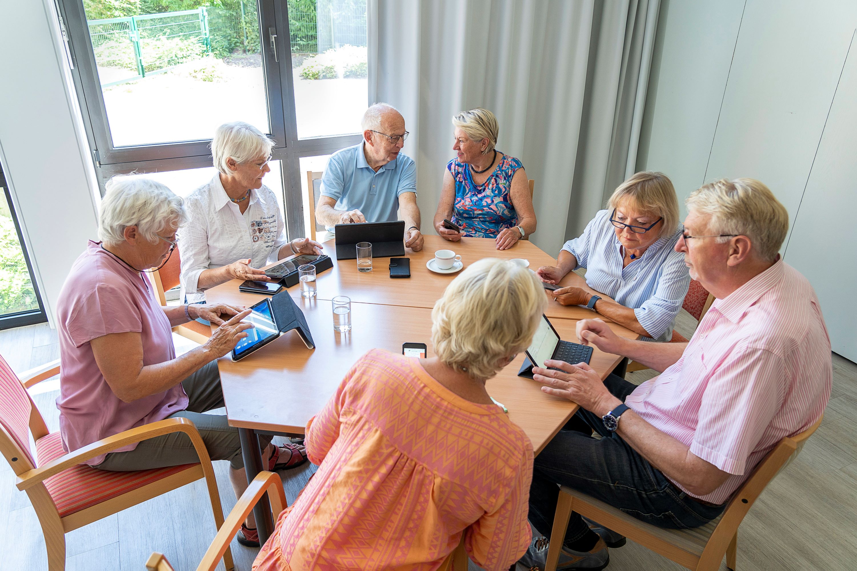 Senioren sitzen rund um einen Tisch und lernen den Umgang mit Tablets