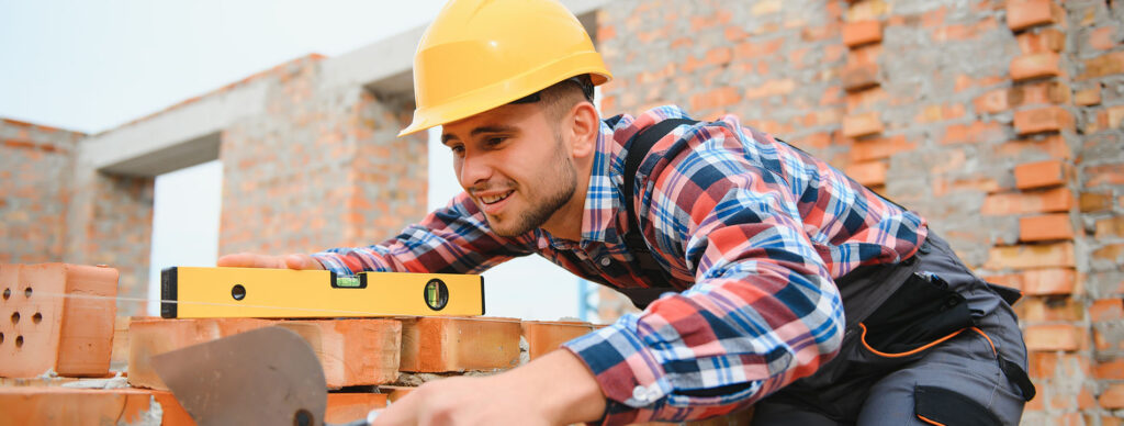 Bauarbeiter mit gelbem Helm auf einer Baus-Baustelle mit gelber Wasserwaage und roten Ziegelsteinen